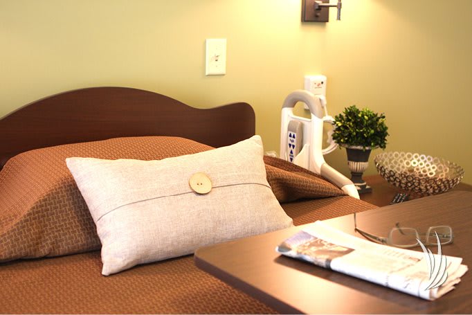 A cozy bedroom setup featuring a neatly made bed with a decorative pillow, adjacent to a nightstand adorned with a plant and reading material.