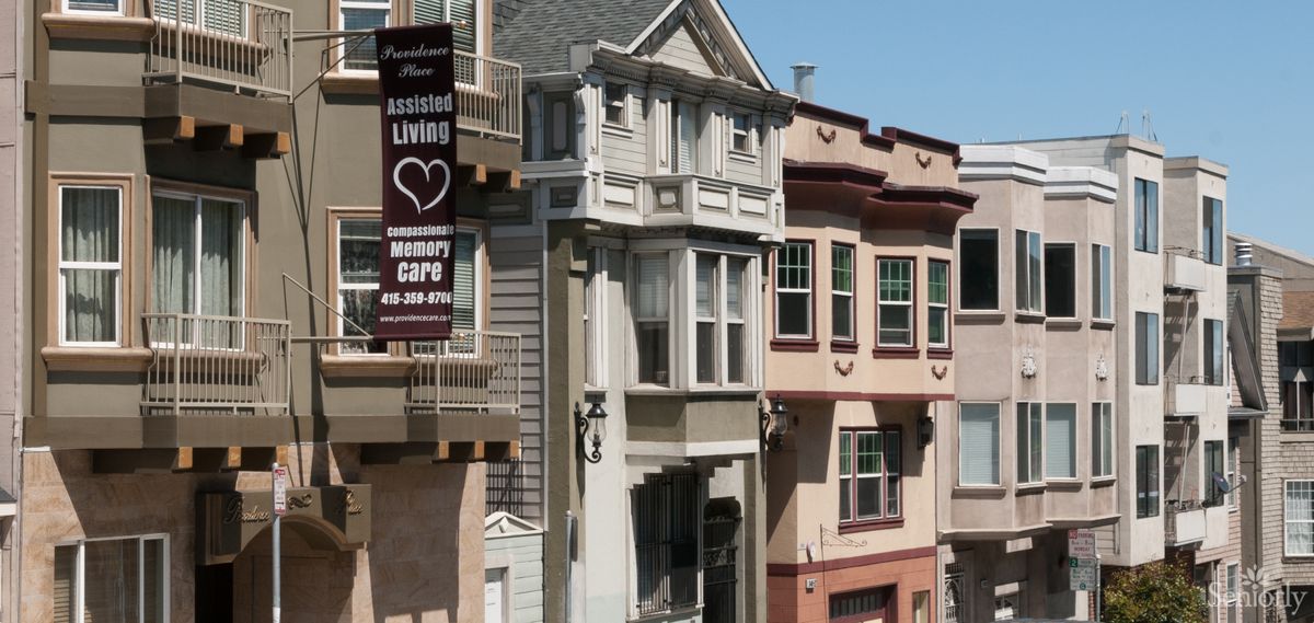 A row of residential buildings with varied architectural styles and a banner advertising senior living.