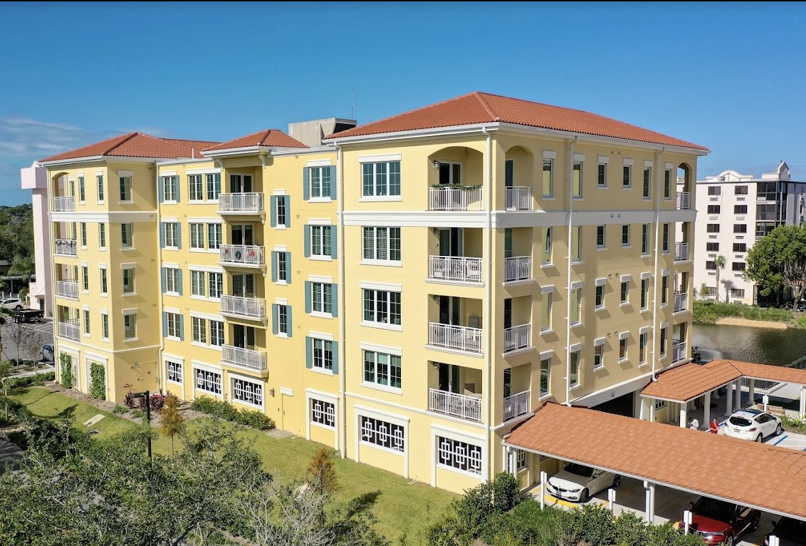 A multi-story apartment building with a yellow facade and red-tiled roof.