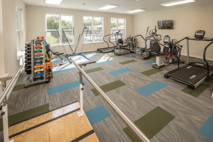 A well-lit gym with various fitness equipment including treadmills, ellipticals, and dumbbells.