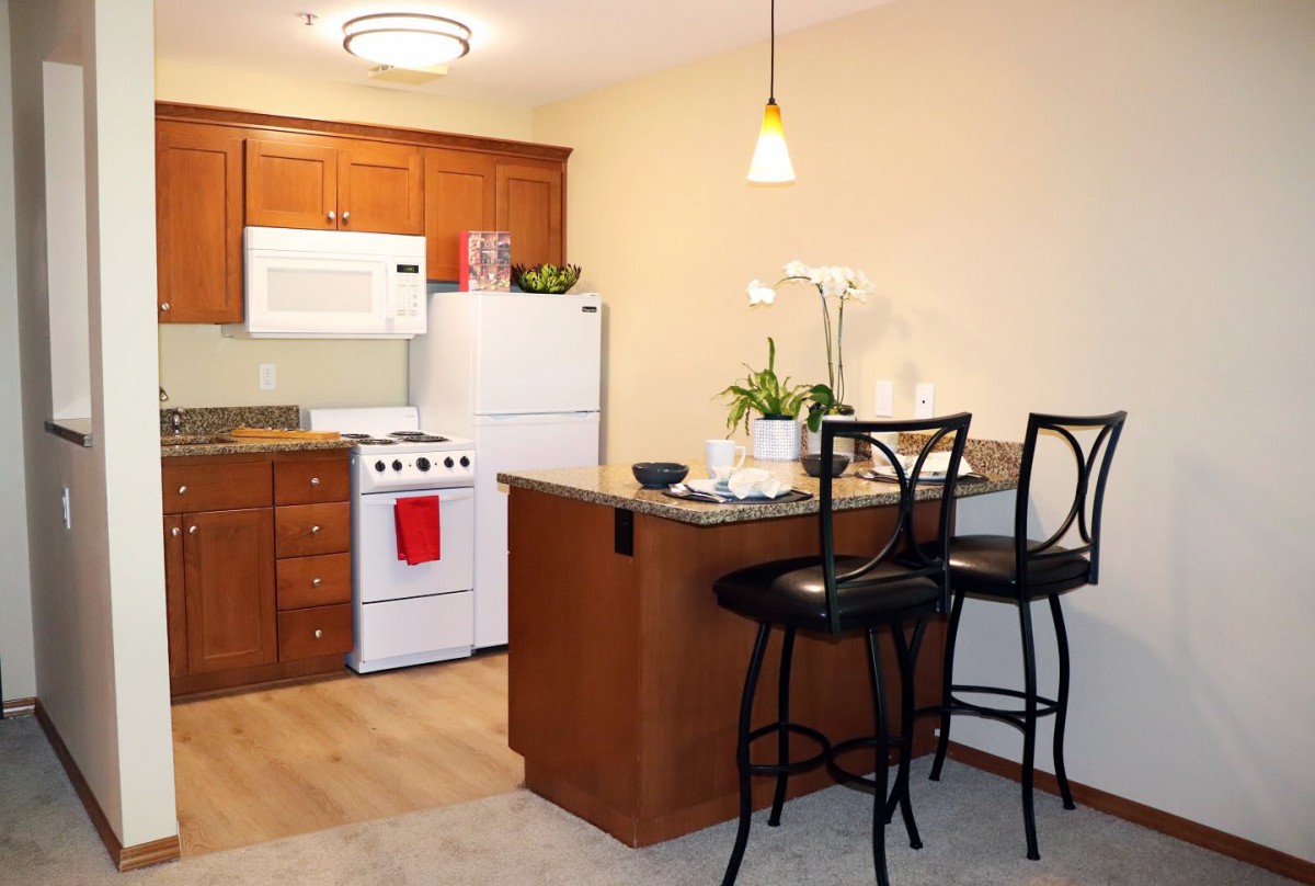 A cozy kitchen with wooden cabinets, a stove, refrigerator, and a small dining area.