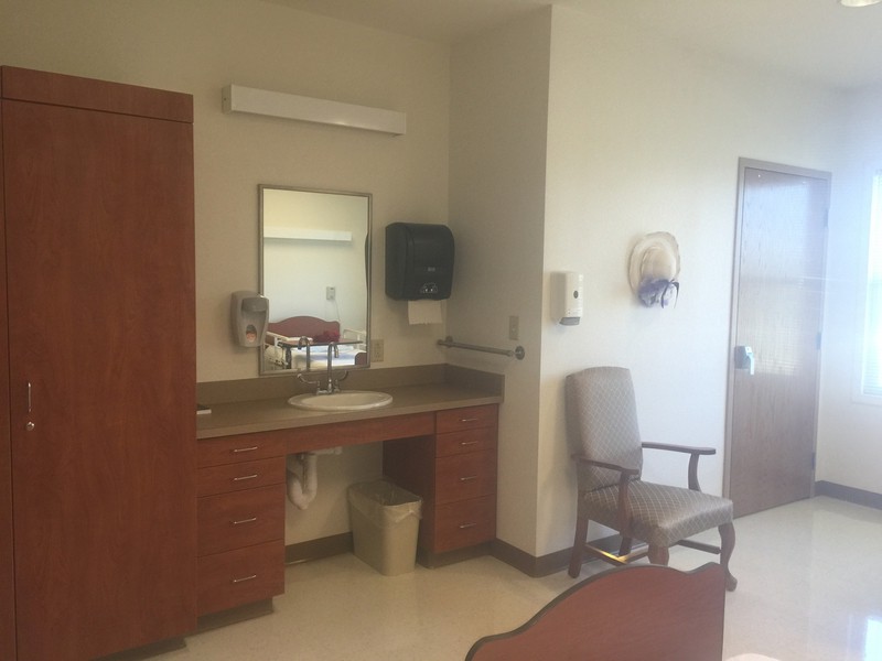 A well-organized hospital room with a sink, chair, and mirror.