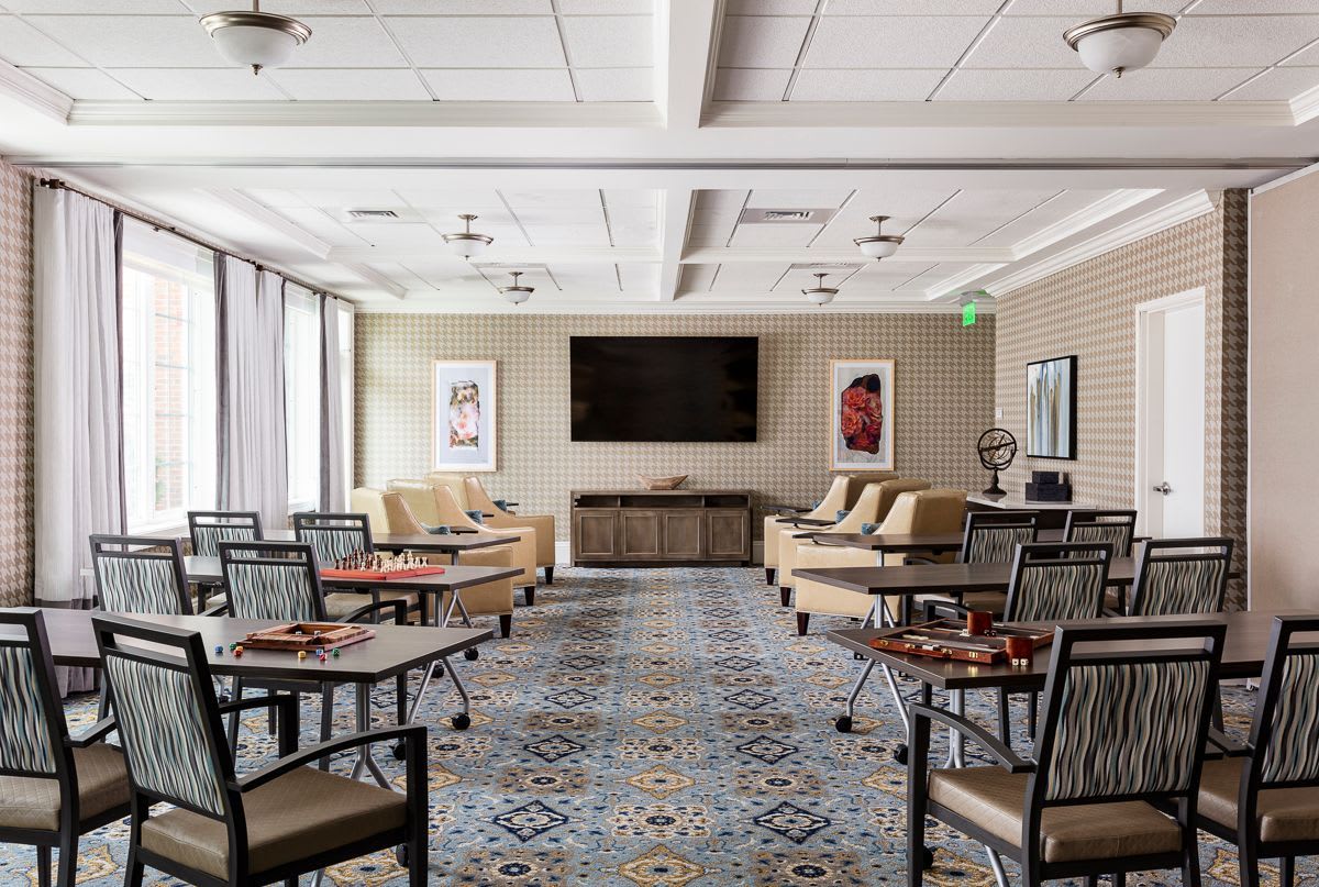 A spacious lounge area featuring tables, chairs, and a large television.