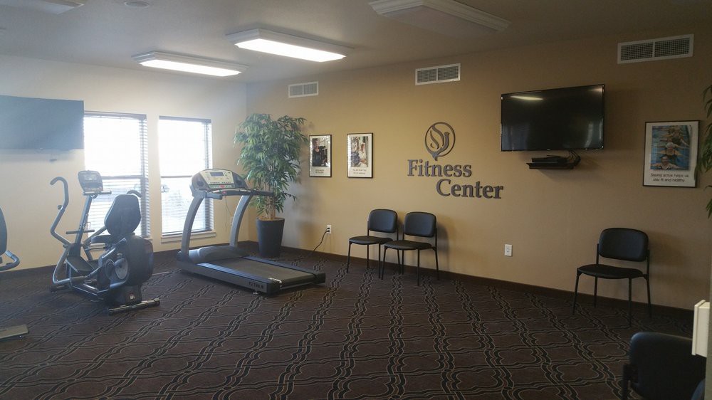A small fitness center with a treadmill, chairs, a potted plant, and a wall-mounted TV.