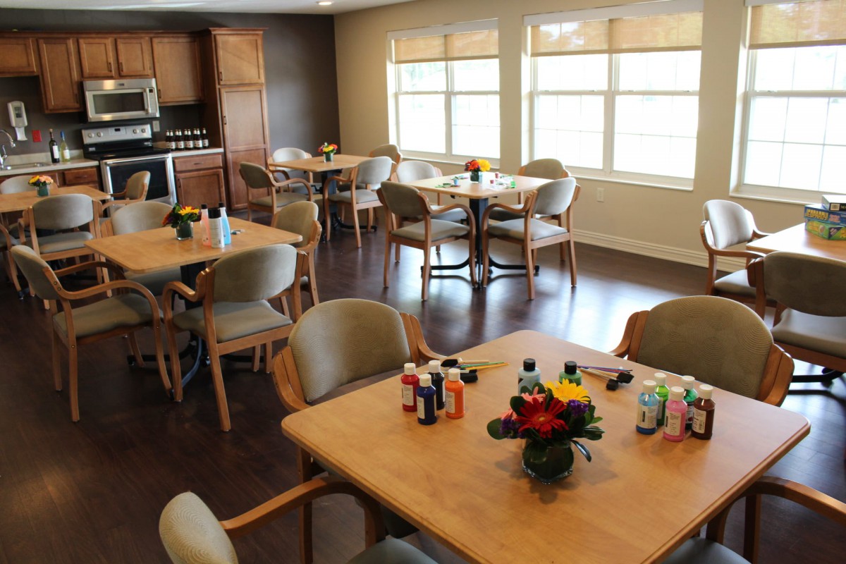 A communal dining and activity area with tables set up for arts and crafts, featuring paint supplies and flower centerpieces.