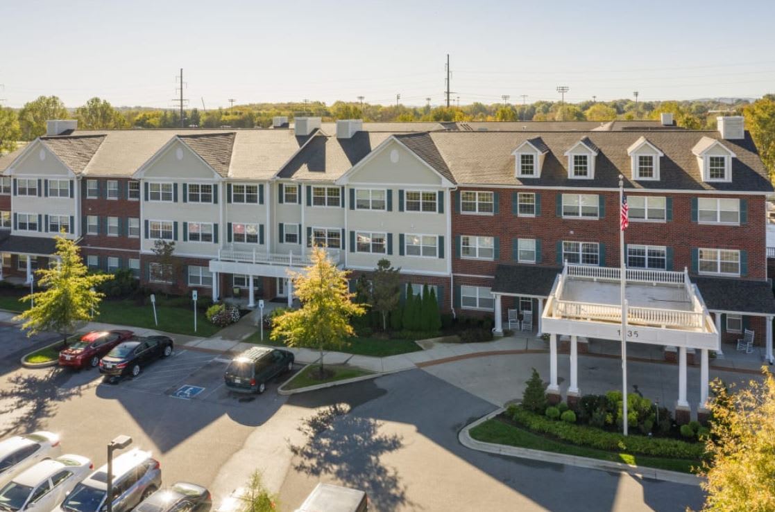 A residential building with a parking lot and surrounding greenery.
