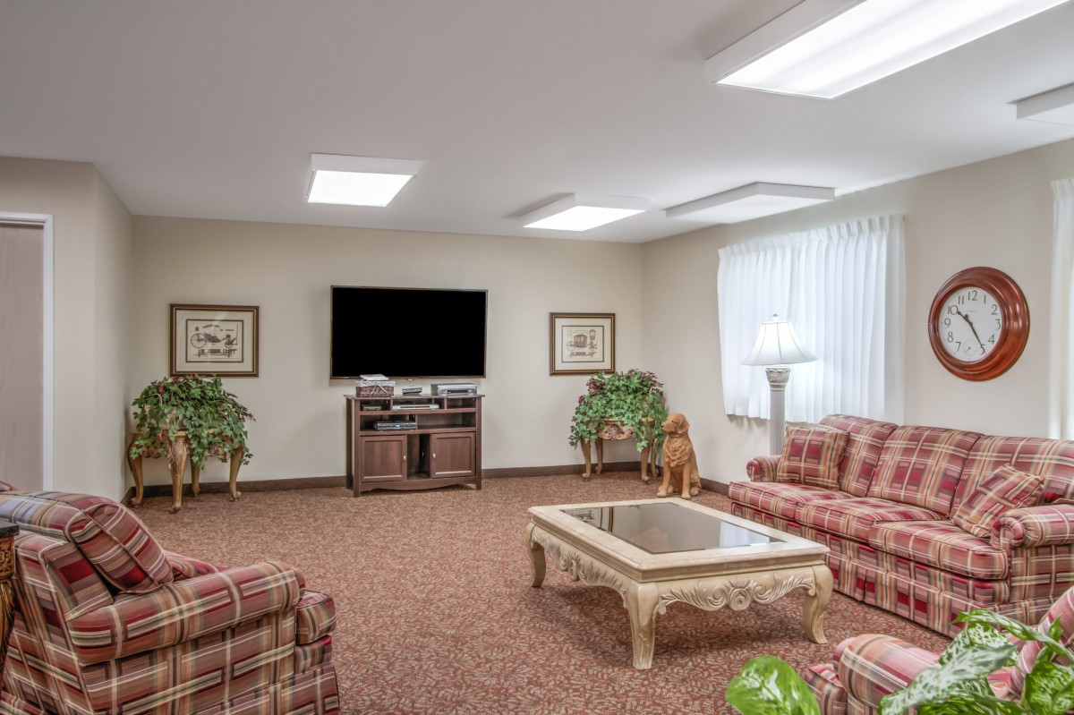 A cozy living room with patterned sofas, a coffee table, and a large television.