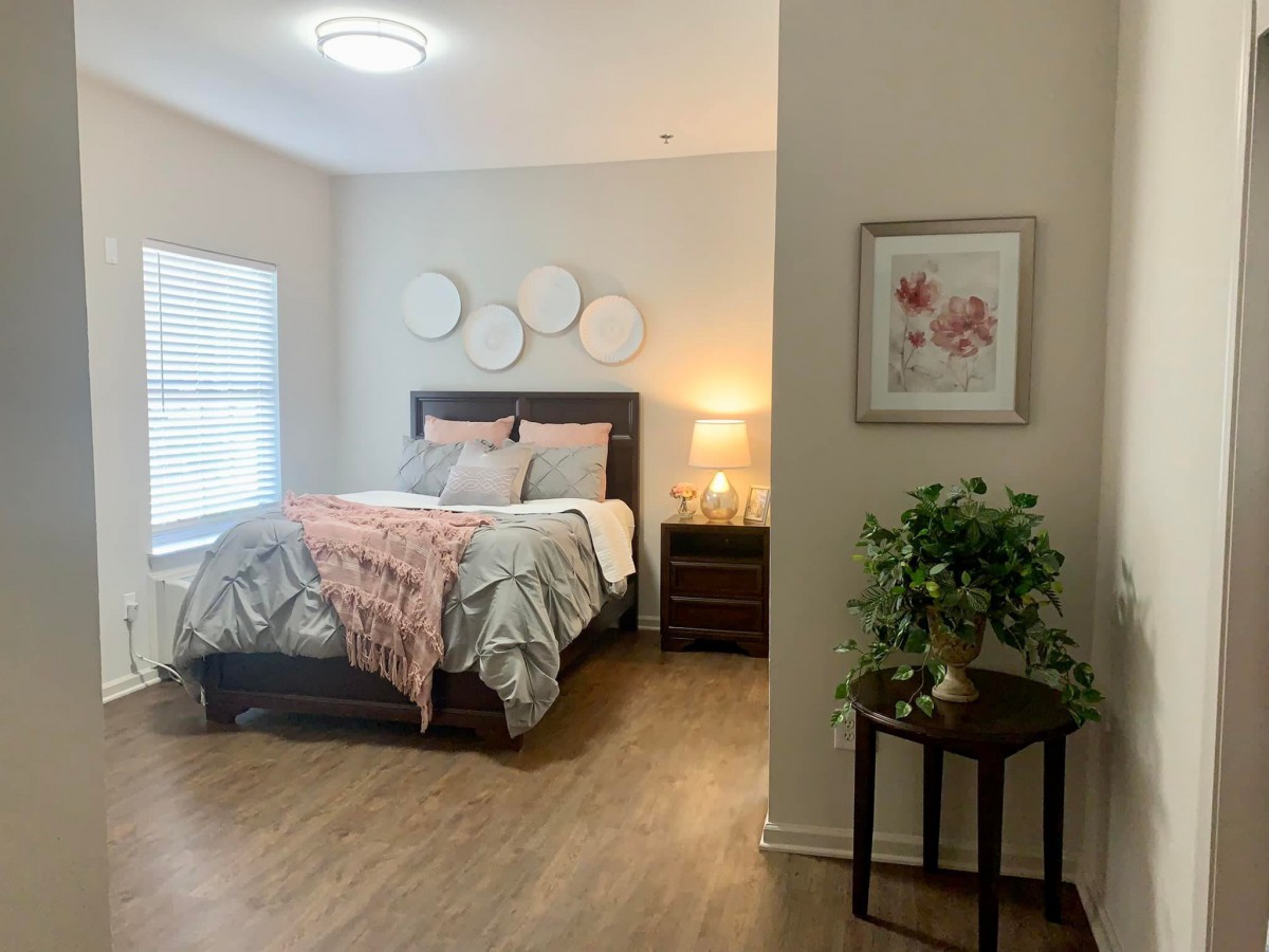 A cozy and well-decorated bedroom with a neatly made bed, a nightstand featuring a lamp, and wall decorations.