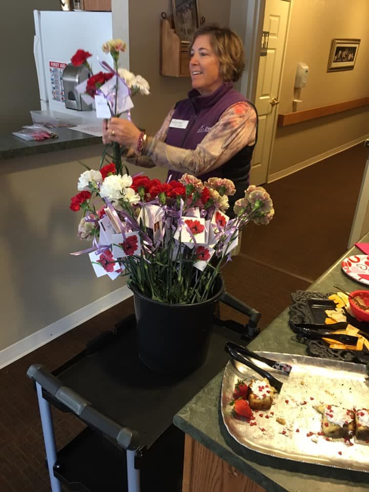 A person arranging a bouquet of red and white carnations in a container indoors.