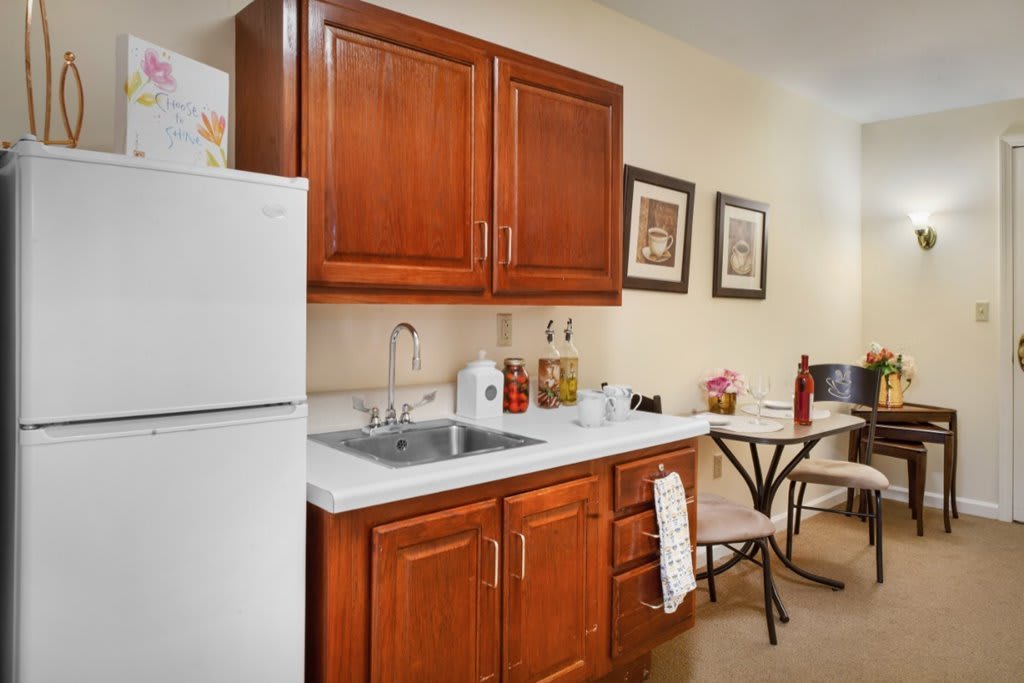 A compact kitchen setup with wooden cabinets, a refrigerator, sink, and a small dining area.