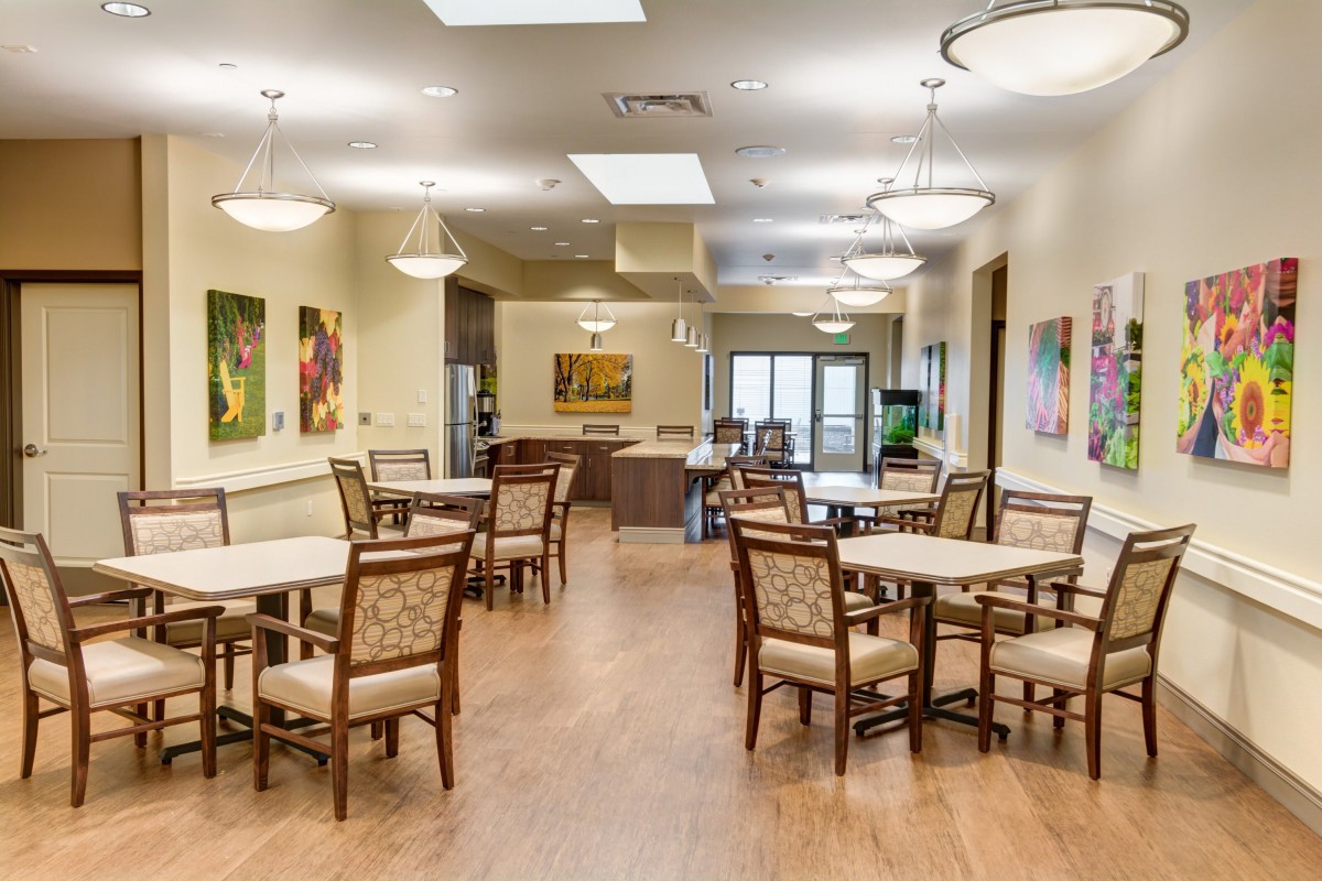 A spacious and well-lit dining area with several tables and chairs, adorned with colorful paintings on the walls.