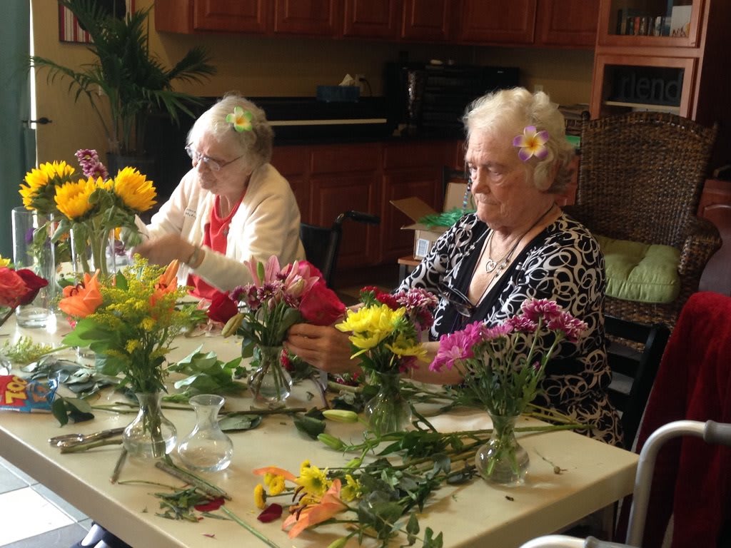 Two elderly women engaged in flower arranging indoors.