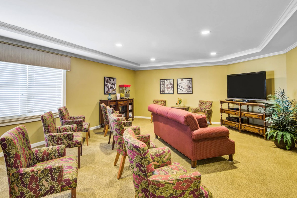 A cozy living room featuring a sofa and several chairs arranged around a television, with decorative artwork on the walls.