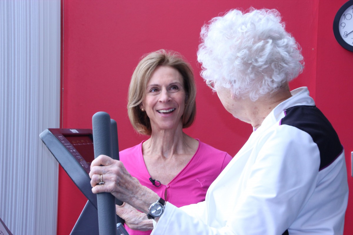 Two women engaging in a conversation while exercising at the gym.