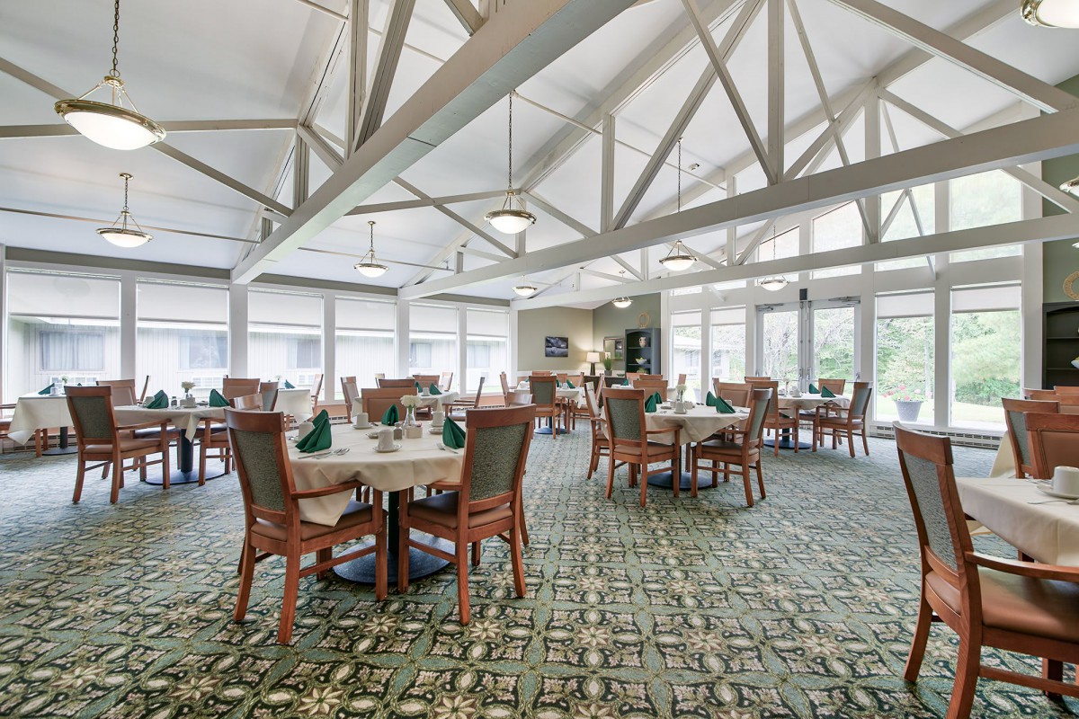 A spacious dining room with neatly arranged tables and chairs, illuminated by natural light from large windows.