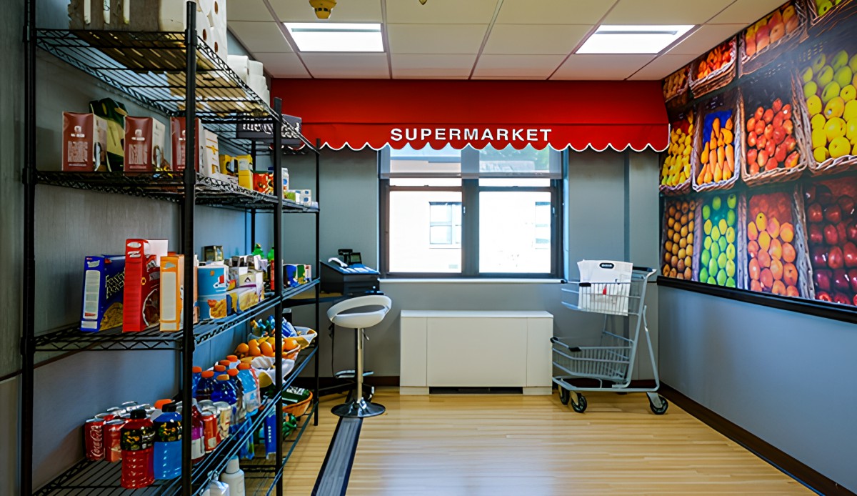 A small indoor supermarket with shelves stocked with various products and a shopping cart.