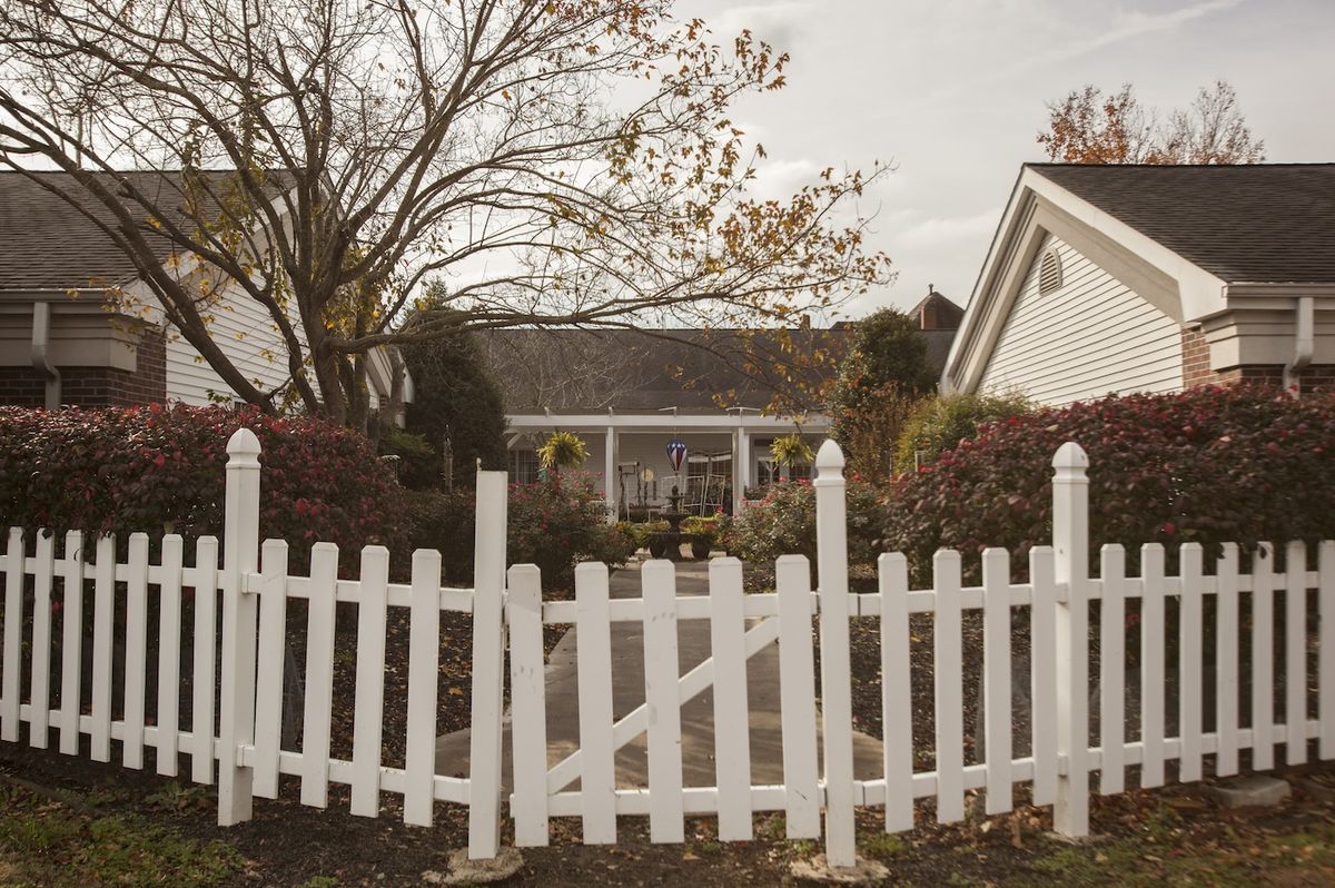 A quaint house with a white picket fence surrounded by autumn foliage.