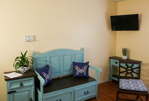 A cozy living room space featuring a light blue bench with decorative pillows, a small plant, and a television mounted on the wall.