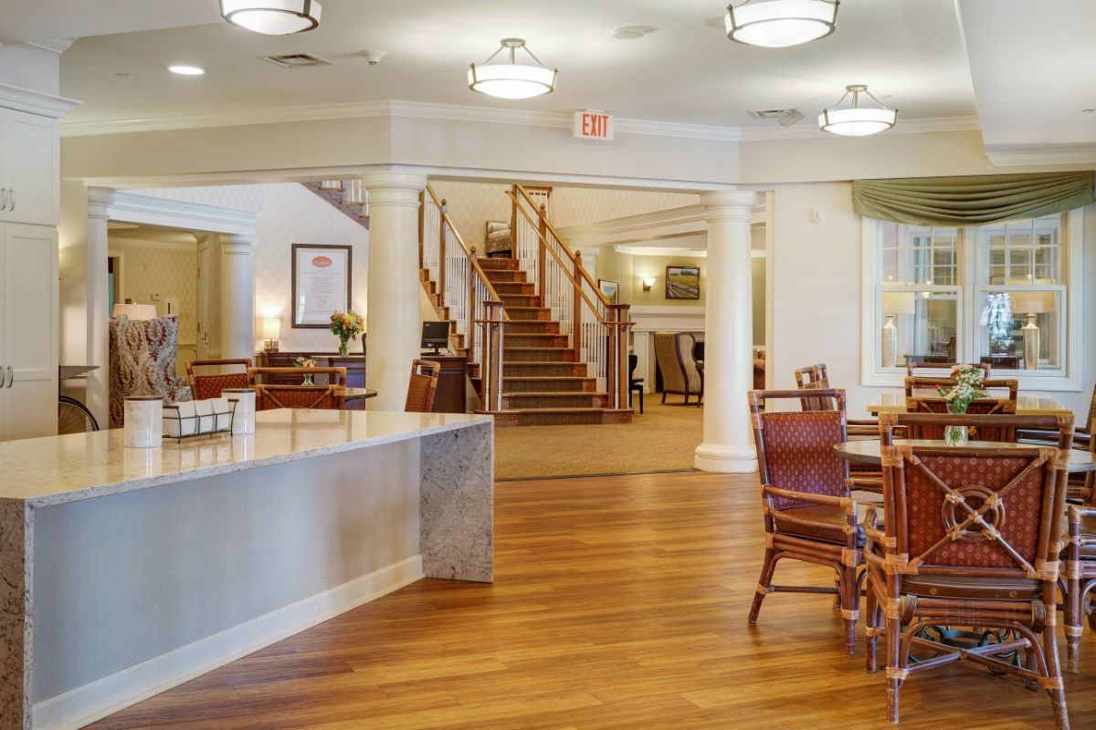 A spacious lobby area with wooden flooring and elegant furniture, featuring a staircase and bright lighting.