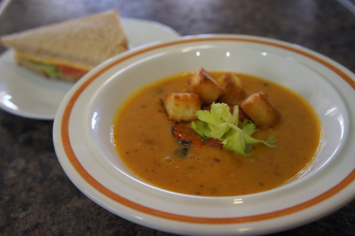 A bowl of soup garnished with croutons and celery, accompanied by a slice of bread.