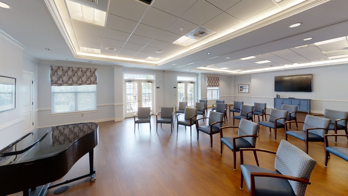 A spacious meeting room with arranged chairs and a piano, featuring large windows and ample lighting.