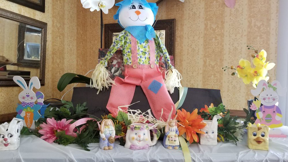 A festive table display featuring a handmade scarecrow, surrounded by ceramic animal figures and colorful flowers.