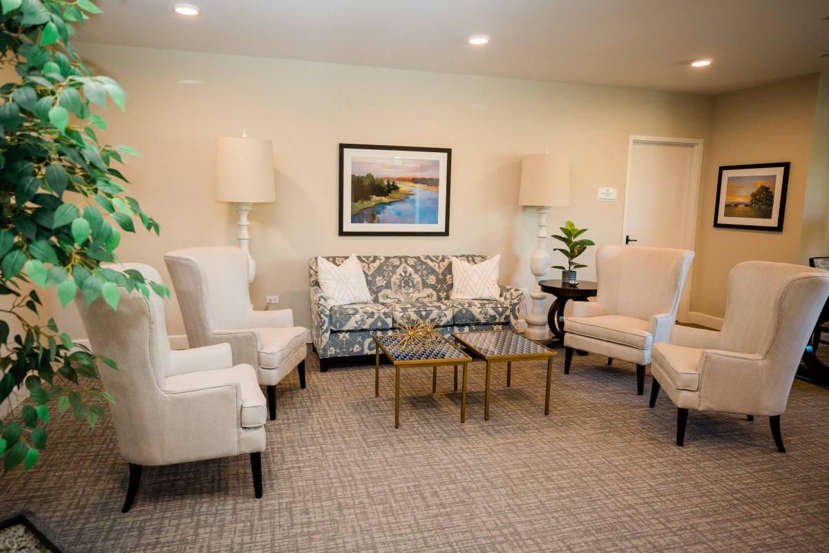 A cozy living room with elegant furniture, including a sofa, armchairs, and a coffee table. The decor features a framed painting and lamps for lighting.