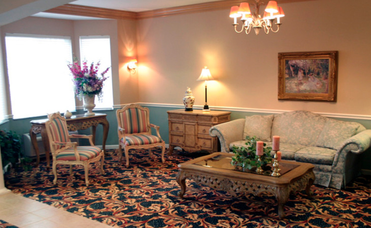A traditionally decorated living room featuring a floral carpet, elegant armchairs, and a chandelier.