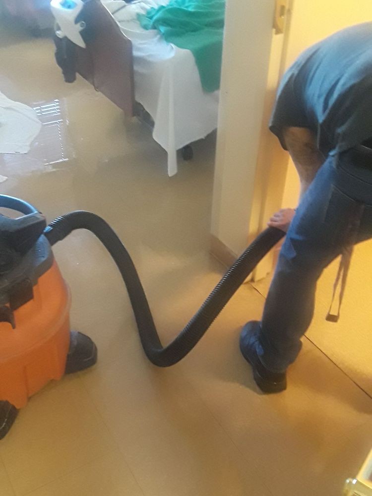 A person uses a vacuum to clean up water after a flood indoors.