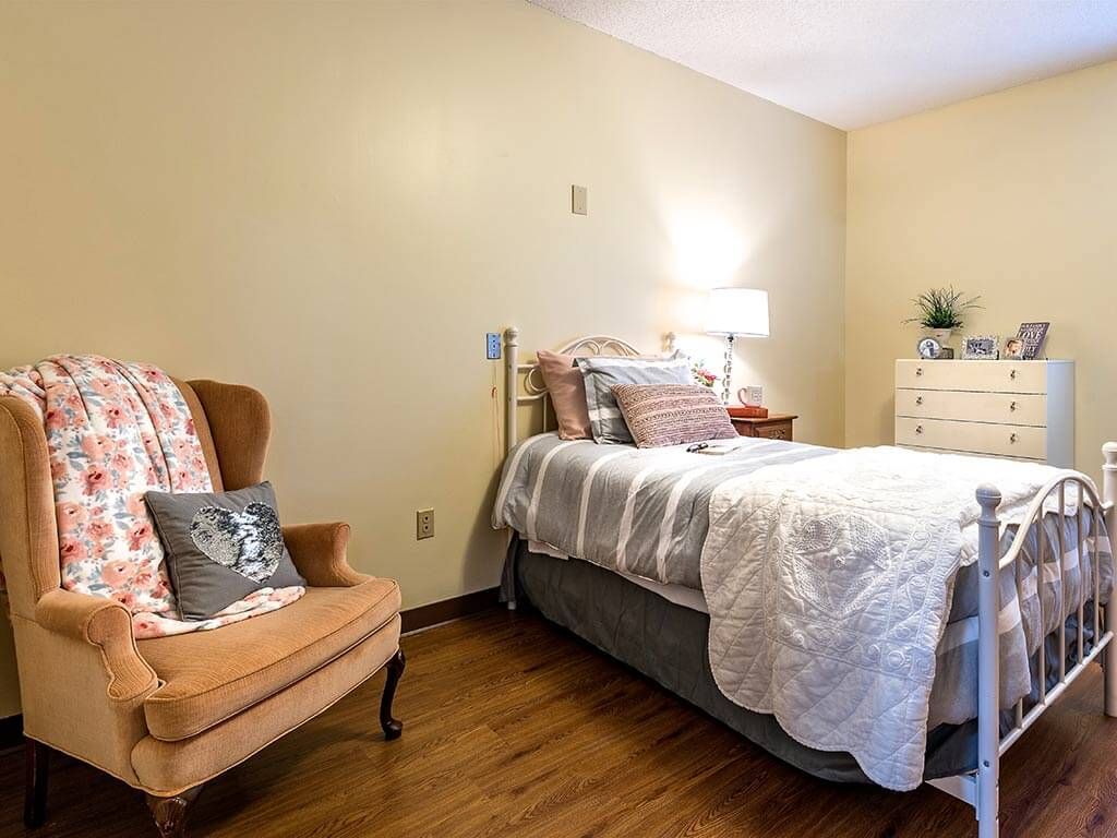 A cozy bedroom with a neatly made bed, an armchair, and a dresser.