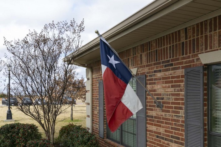 A Texas flag is mounted on a brick house under a cloudy sky.