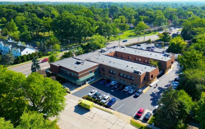 An aerial view of a brick office building surrounded by trees with a parking lot in the foreground.
