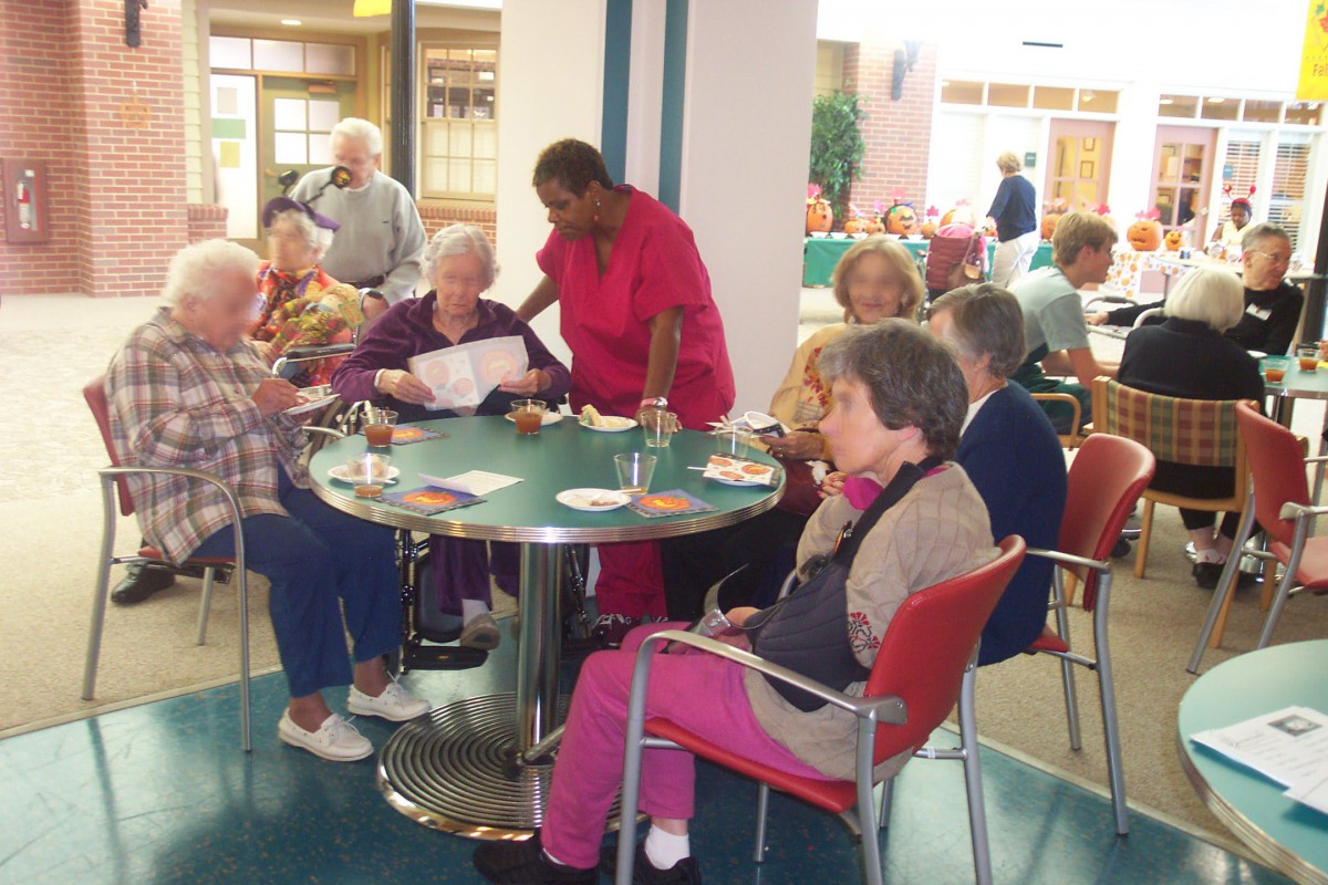 A group of elderly individuals seated around a table in a communal setting, engaging in conversation and activities.