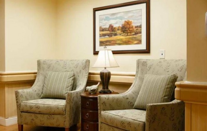 A cozy living room setup featuring two armchairs, a side table with a lamp, and a landscape painting on the wall.