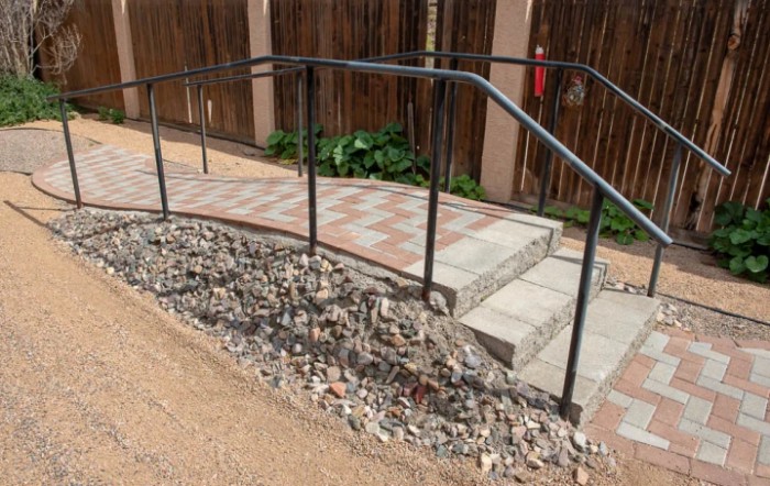 An outdoor ramp with a handrail, bordered by gravel, leading to a brick walkway.
