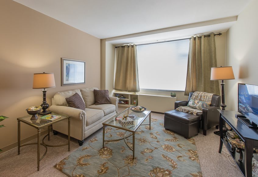 A cozy living room with a sofa, armchair, and coffee table, tastefully decorated with lamps and a rug.