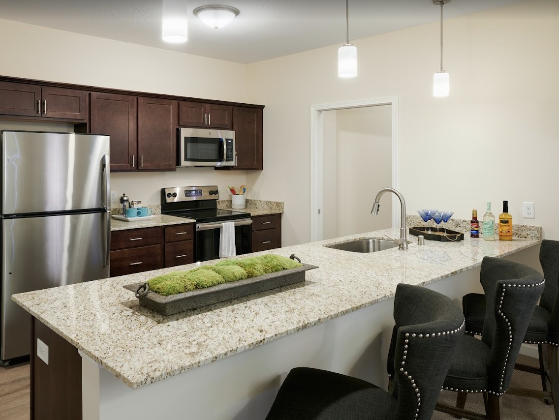 A modern kitchen featuring stainless steel appliances, a granite countertop island with bar stools, and pendant lighting.