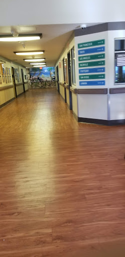 A view of a hospital hallway with wooden flooring, featuring multiple doors and directional signs.