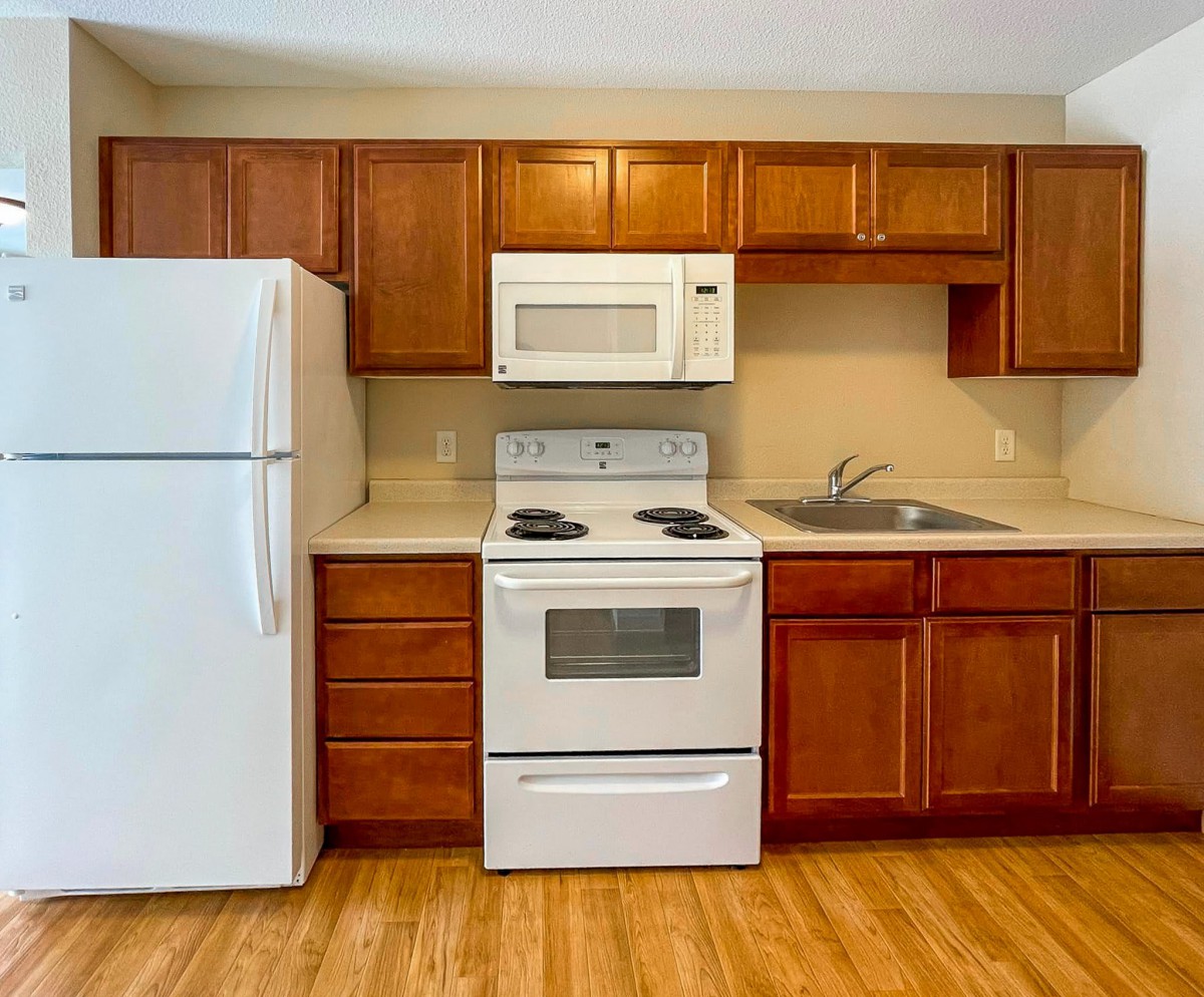 A modern kitchen with wooden cabinets, featuring a refrigerator, oven, microwave, and sink.