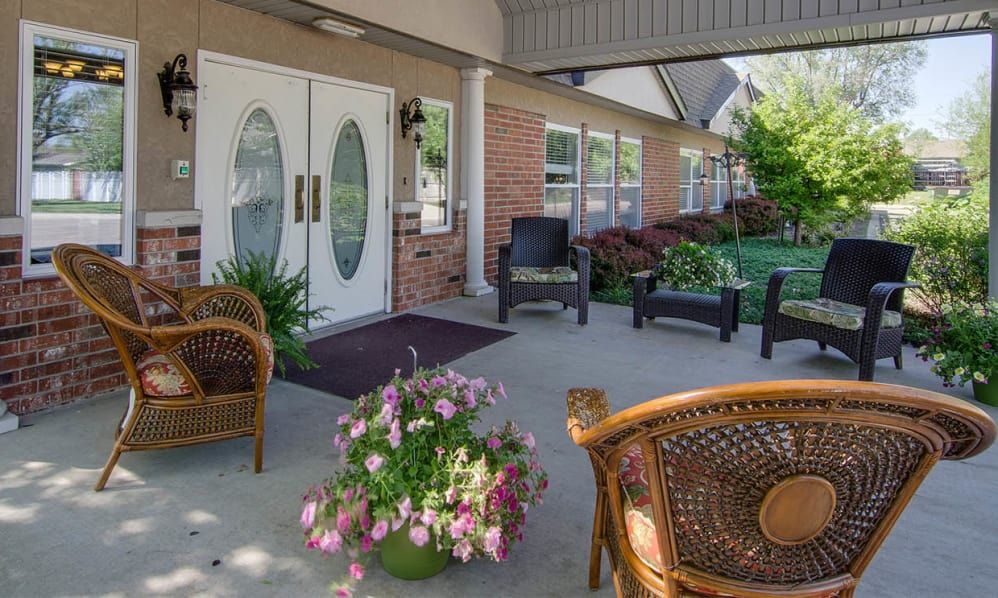A cozy porch with wicker chairs, potted flowers, and a building entrance.