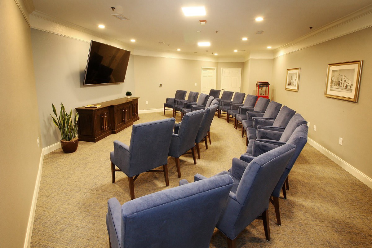 A meeting room with blue chairs arranged in a curved formation facing a large television.