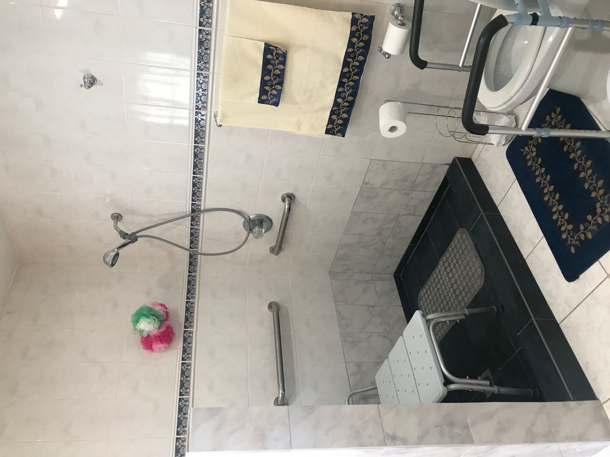 A bathroom with a shower, glass door, and various fixtures such as grab bars and a towel rack.