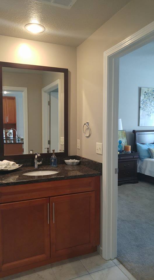 A view from a bathroom into a bedroom, featuring a sink with a mirror and adjacent sleeping area.