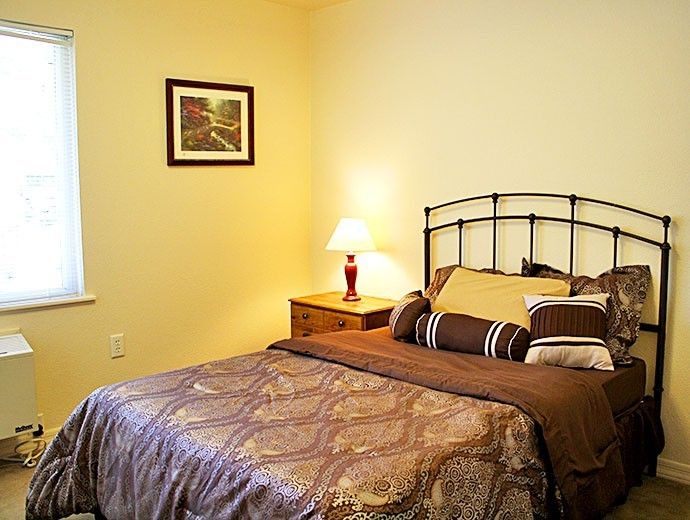 A cozy bedroom with a neatly made bed, a bedside table, and a lamp providing warm lighting.