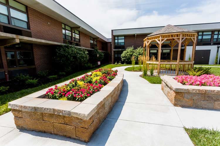 A beautifully landscaped outdoor garden area with colorful flowers, a gazebo, and a brick building in the background.
