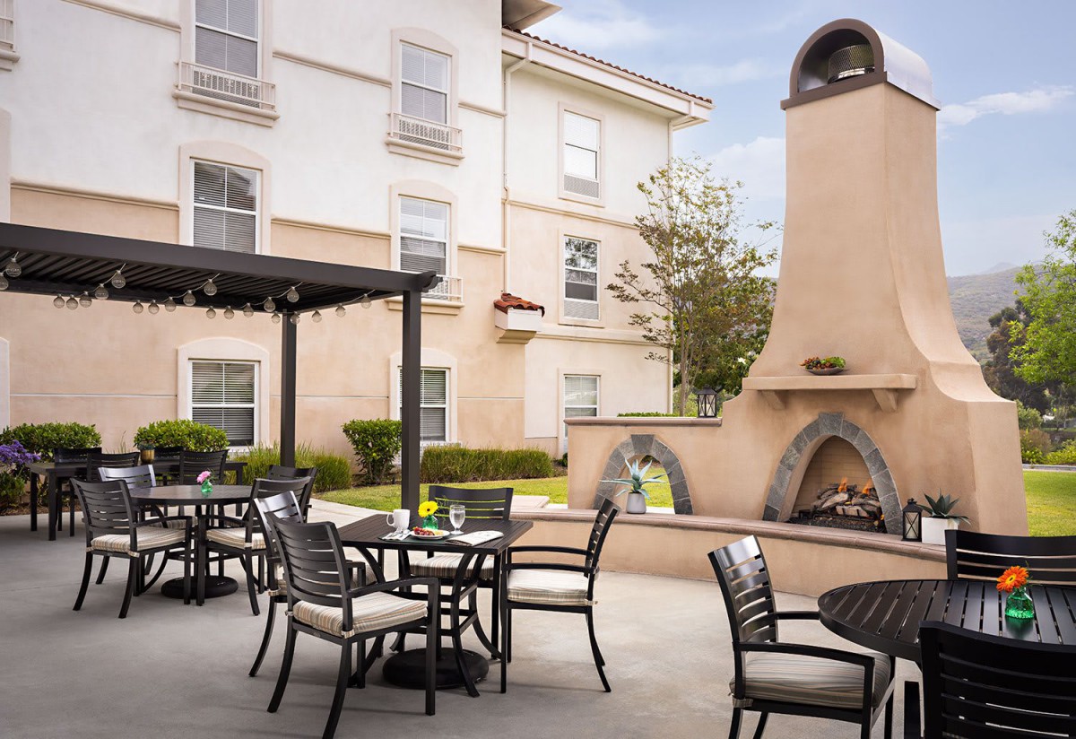 A cozy outdoor patio area with tables, chairs, and a fireplace next to a building.