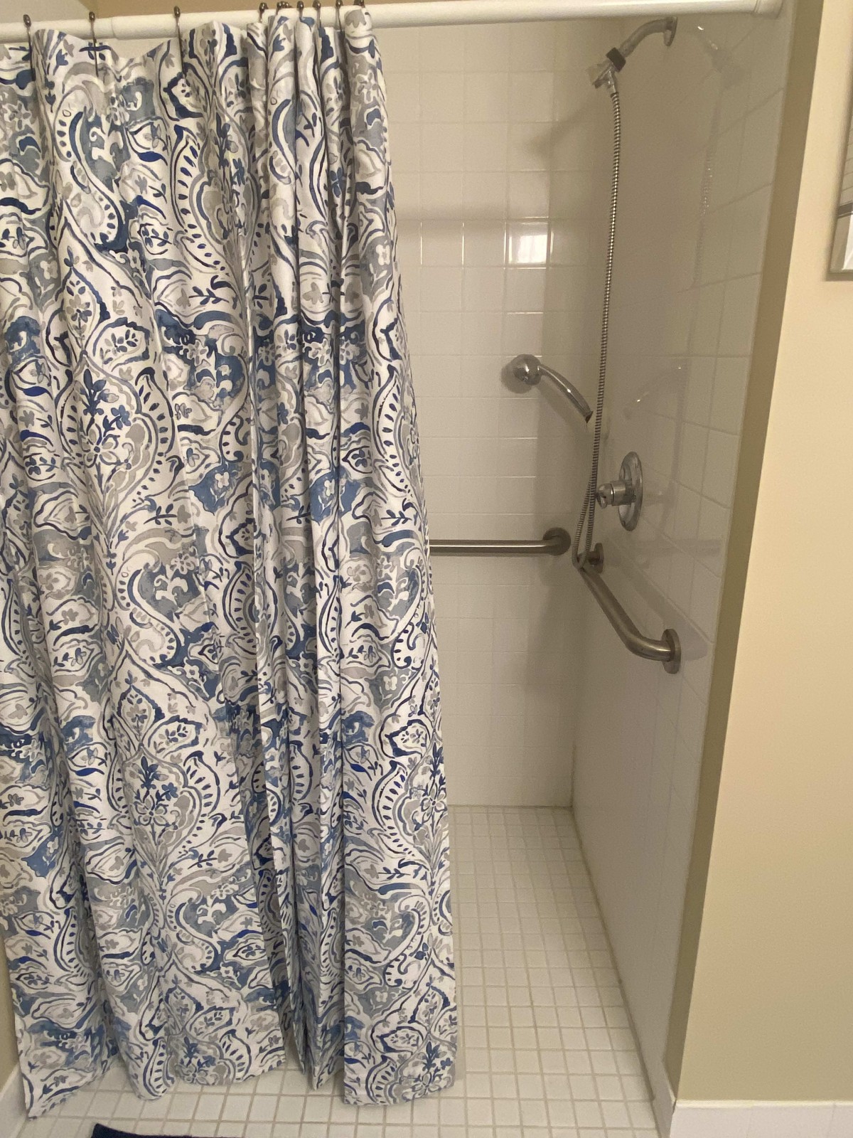 A bathroom shower with a floral-patterned curtain and safety grab bars.