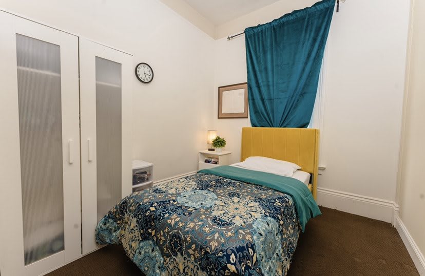 A cozy bedroom with colorful bedding, a yellow headboard, and a blue curtain.