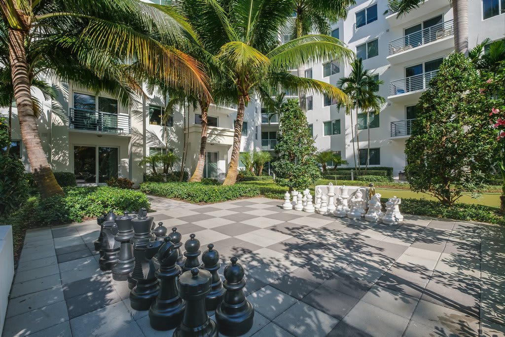 A tranquil garden space with a giant chess set in the courtyard of an apartment building, surrounded by lush palm trees.