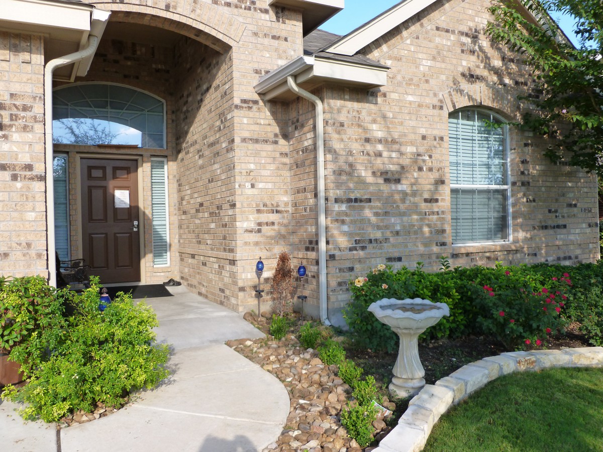 A brick house with a landscaped front yard featuring a walkway and birdbath.